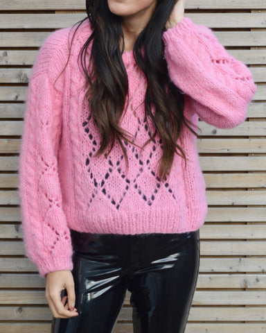 Woman wearing pink lace mohair jumper and black patent trousers next to fence