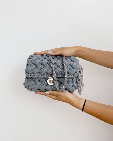 Grey crochet handbag with silver chain and silver clasp held between two hands