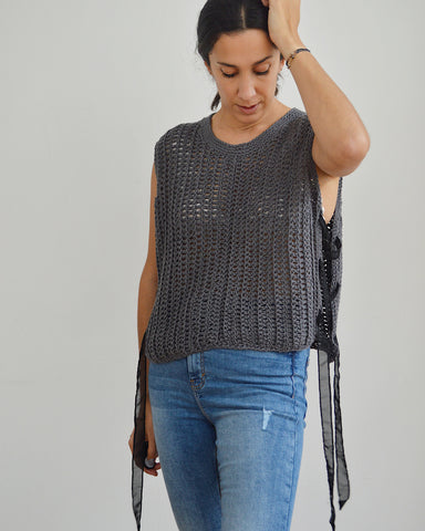 Woman wearing grey crochet vest with black ribbon laced sides and blue jeans