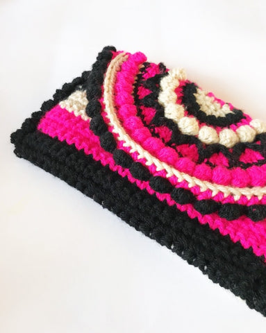 Neon pink, black and cream crochet handbag lying on light surface