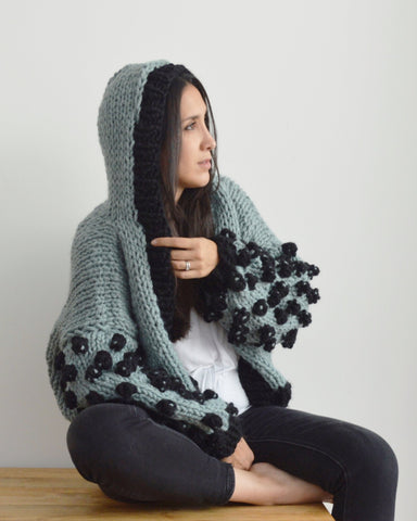 Woman wearing pale green and black hoodie in chunky knit with black bobbles on sleeves