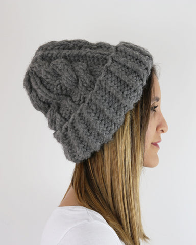 Side view of woman wearing grey cable knit hat against light background