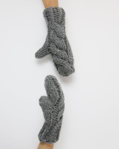 Two hands wearing grey cable knitted mittens against white background
