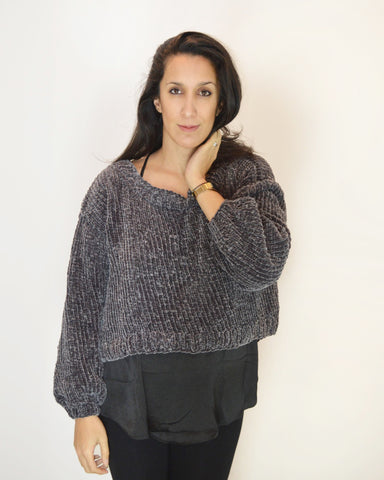 Woman wearing grey velvet sweater with hand on neck against white background