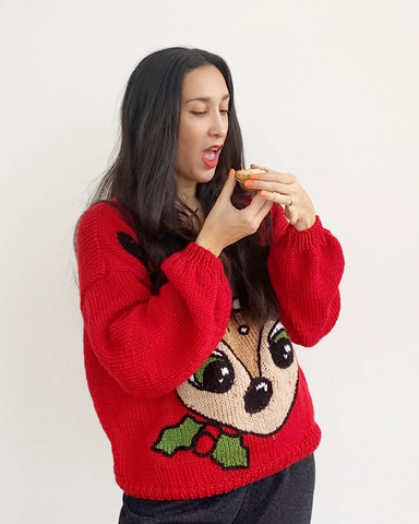 Woman with dark hair wearing red christmas jumper with reindeer image on front, eating mince pie