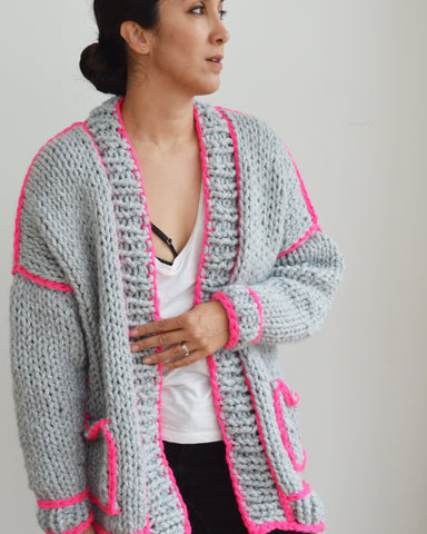 Woman standing wearing grey chunky knit cardigan with neon pink outlines